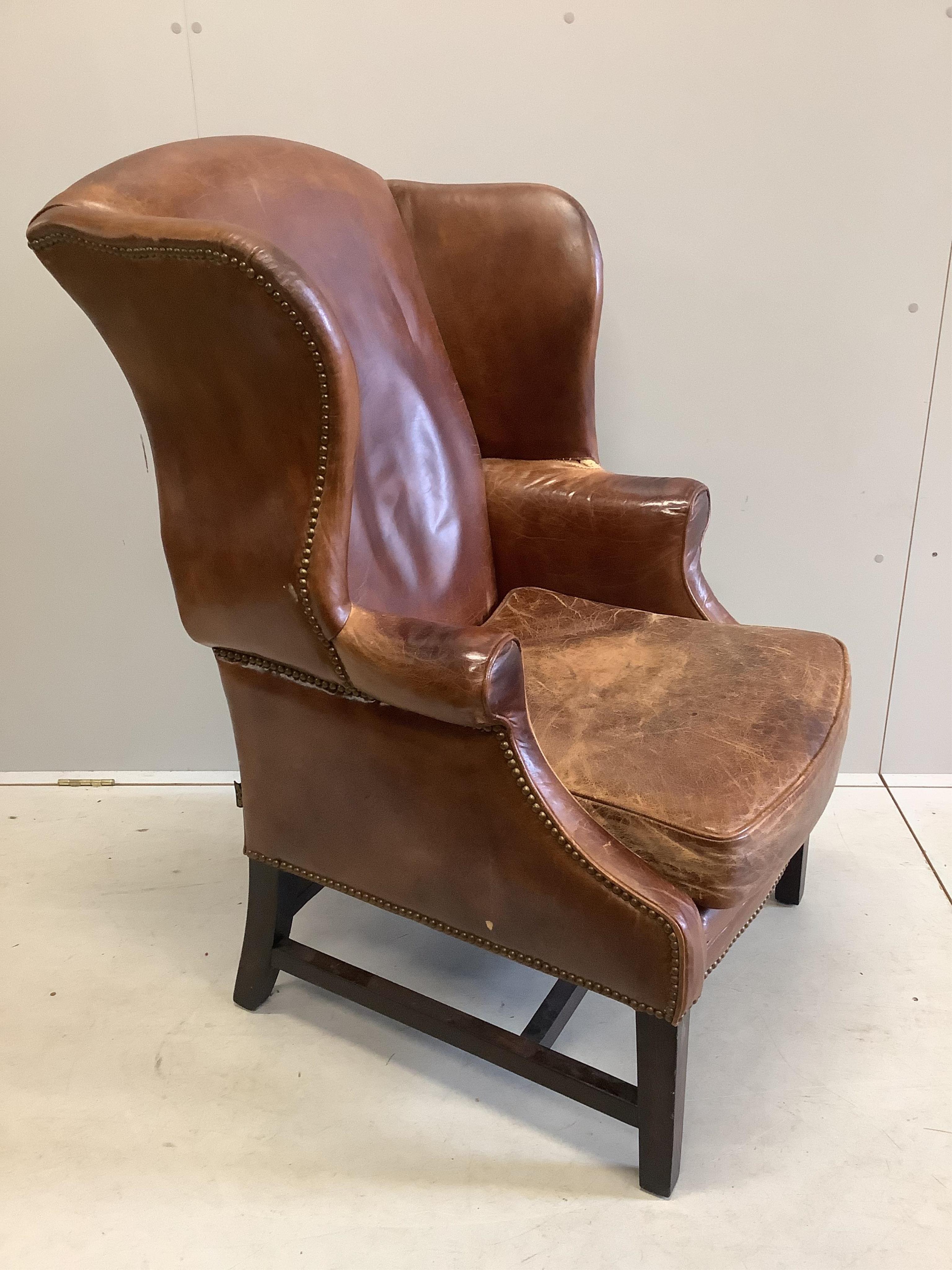 A George III style oak and tan leather wing back armchair, width 76cm, depth 70cm, height 112cm. Condition - poor to fair